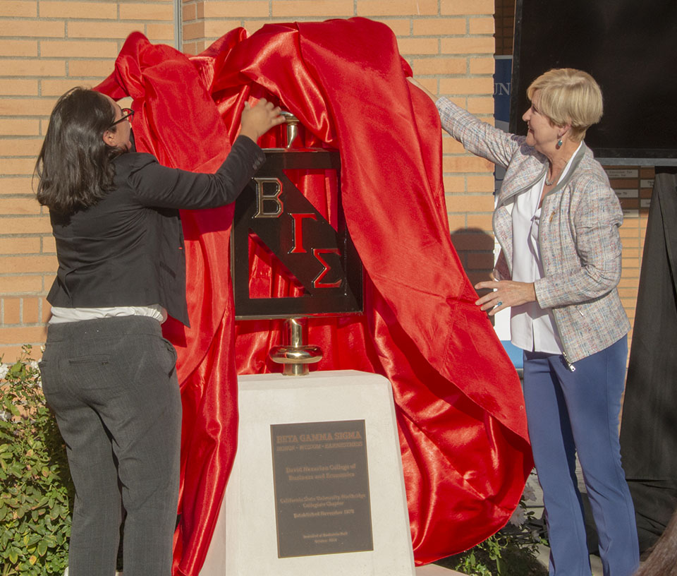 Provost Mary Beth Walker and a Nazarian College business student lift a red drape off of the Beta Gamma Sigma "Bronze Key" sculpture in front of CSUN's Bookstein Hall.
