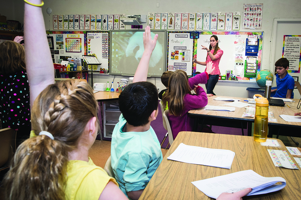 Alumna and teacher Erica Rood stands at the front of her third grade classroom, while CHIME Institute students raise their hands to answer a question.