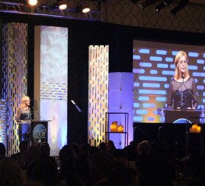 CSUN President Dianne F. Harrison at an LAEDC podium, with her image projected on the big screen, at the 2019 Eddy Awards gala dinner. 