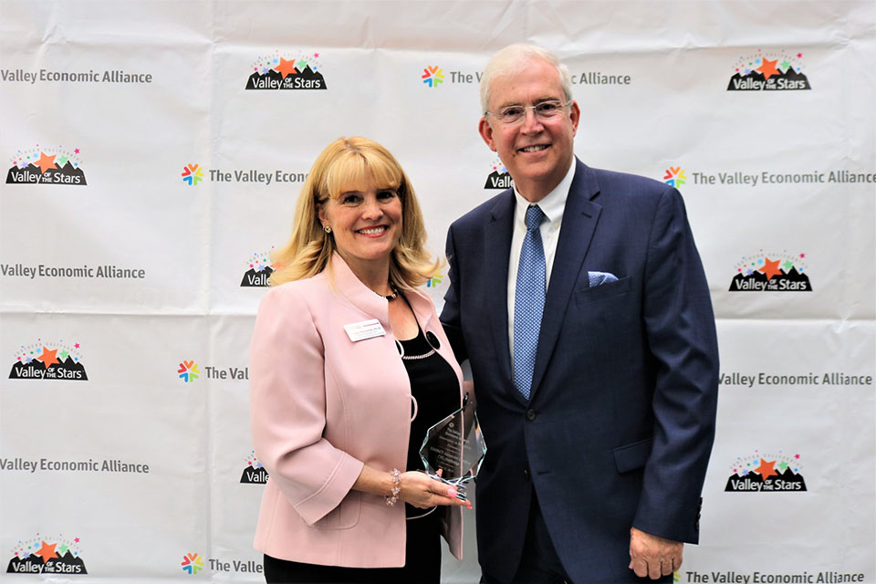 CSUN faculty member Wendy Murawski and LA Economic Development Corporation CEO Bill Allen stand in front of a Valley Economic Alliance step-and-repeat, while Murawski holds a glass award from the alliance.