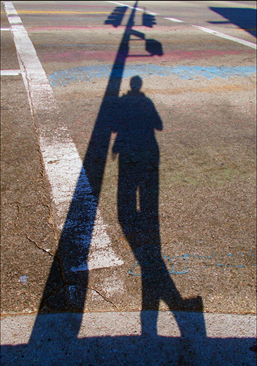 A silhouette of a person leaning against a traffic light pole.