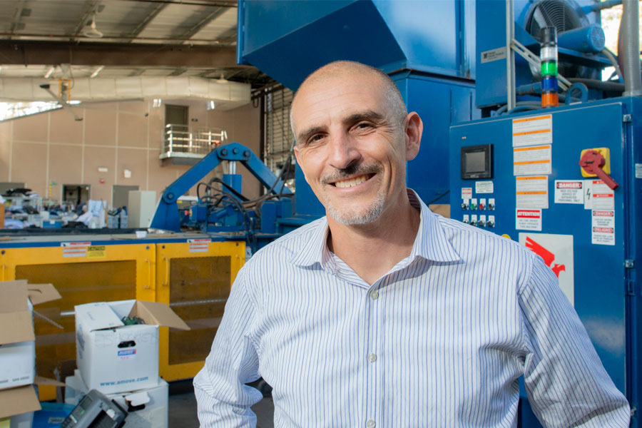 Natale Zappia is in a blue button-up shirt posed in front of blue industrial machinery.