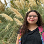 CSUN student Emily Gomez stands in front of plants and identifies as Ojibwe and Guatemalan.