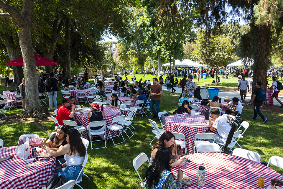 Students sitting at tables with red-checkered tablecloths on the Bayramian Hall lawn.