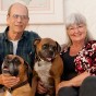 Dr. Richard and Ilona Buratti sitting on their couch at home with their beloved boxers, Travis (who is in between them on the couch) and Phoebe (in front of them).