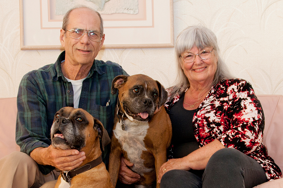 Dr. Richard and Ilona Buratti sitting on their couch at home with their beloved boxers, Travis (who is in between them on the couch) and Phoebe (in front of them).