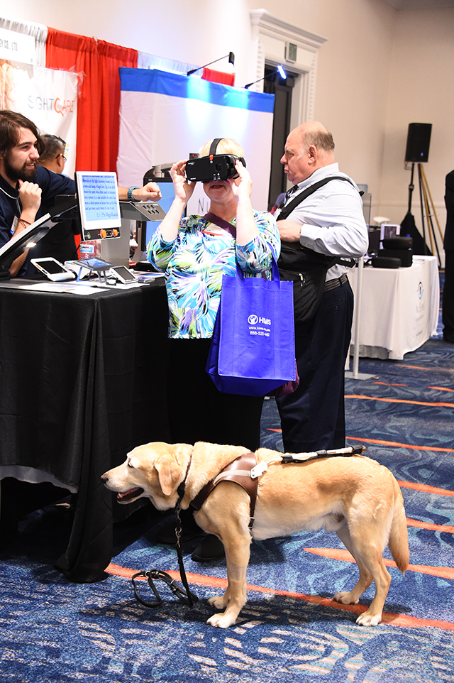 A woman with a service dog tries vision-enhancing glasses at the CSUN Conference.