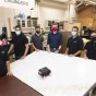 A group of students wearing masks standing up around a white table where there is a robot at the center.