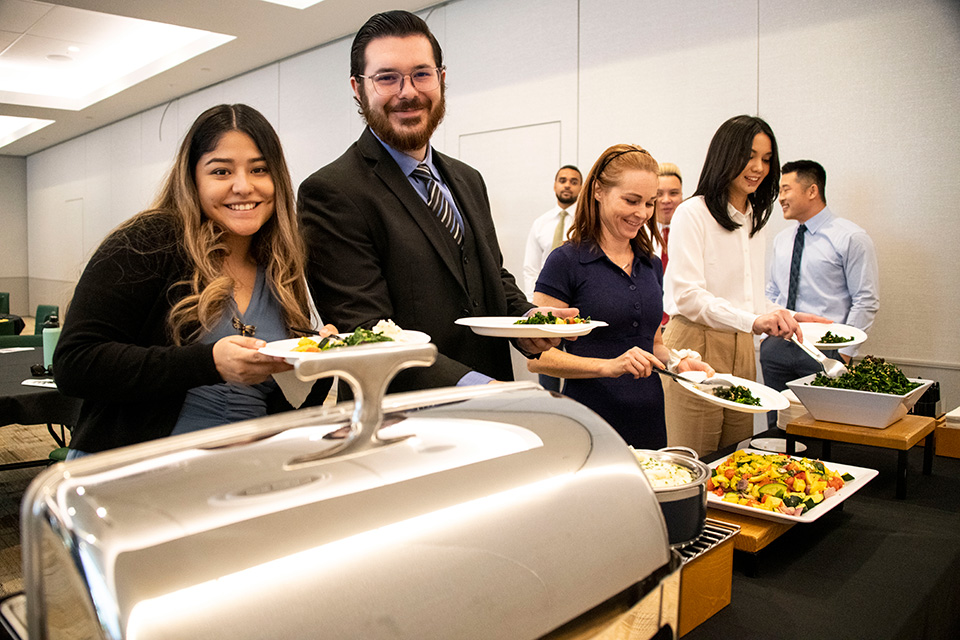 Students standing behind buffet with plate in hand, smiling.