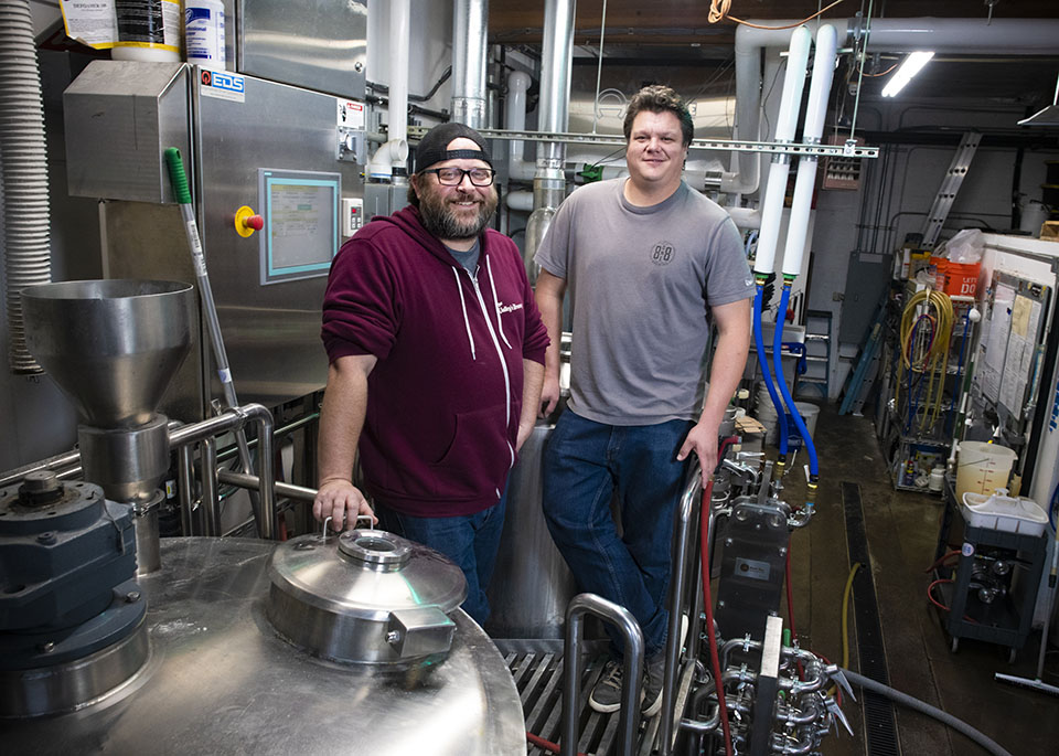 Cousins Bryan and Derrick Olson stand next to to their beer tanks and brewing equipment, where 8one8 beer is made.