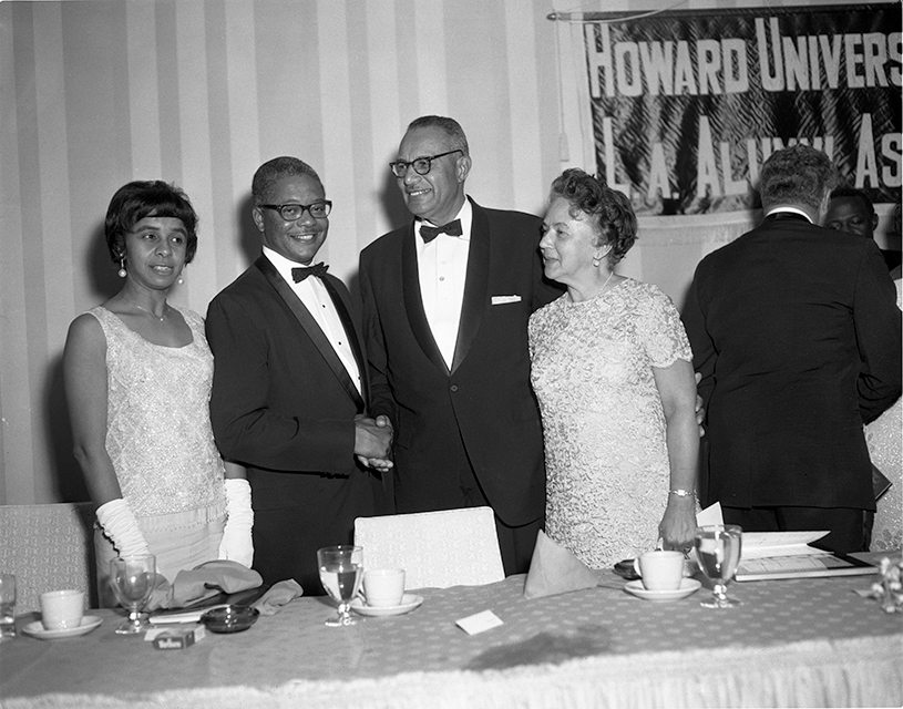 Four Howard University alumni in formal wear stand behind a table at an alumni event.