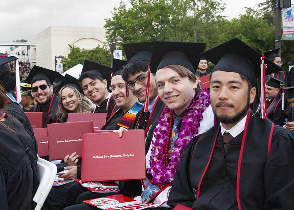 A line of graduates hold up their diplomas at the 2019 CSUN commencement.