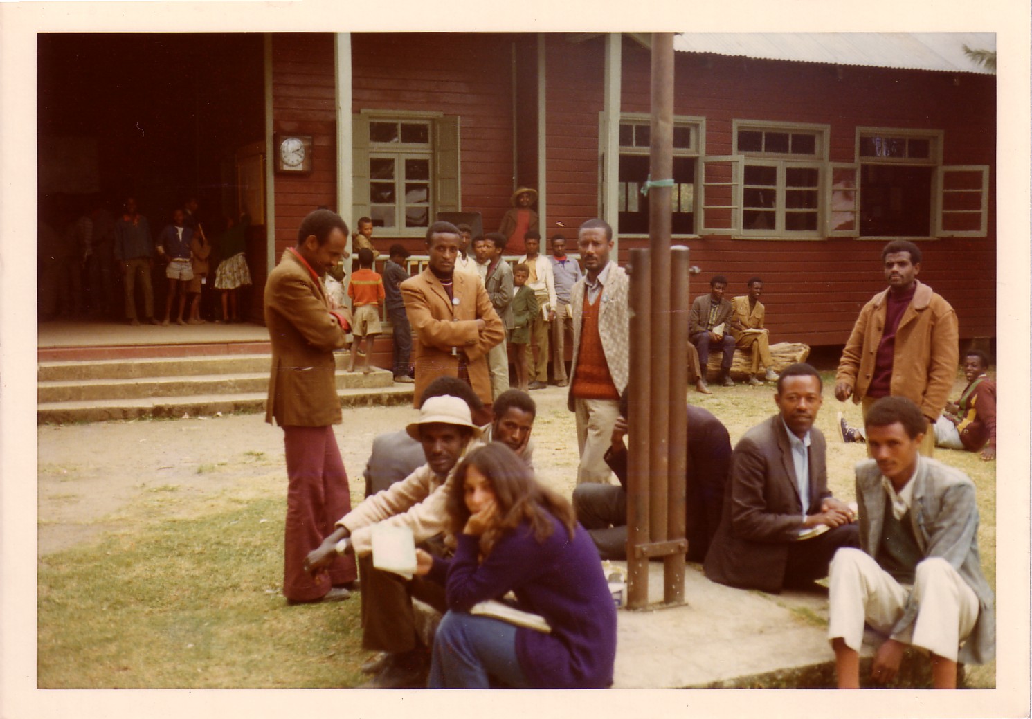 Andi Ostrowe sits outside a building, surrounded by several men.