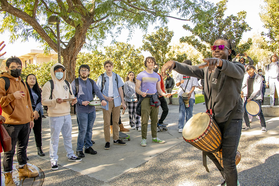 Curtis Byrd wearing a drum, gestures to the crowd of students gathered behind him.