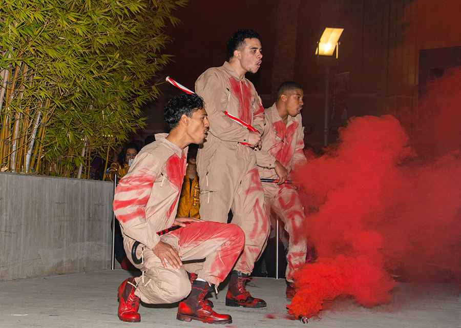 Kappa Alpha Psi Fraternity members perform behind red smoke.