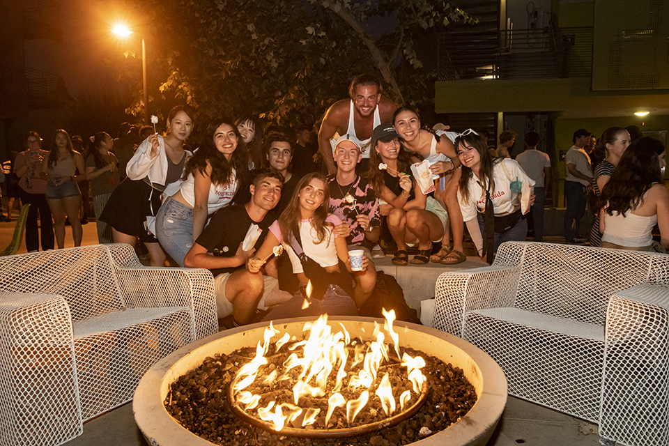 Large group photo of students sitting in front of a fire in a fire pit.