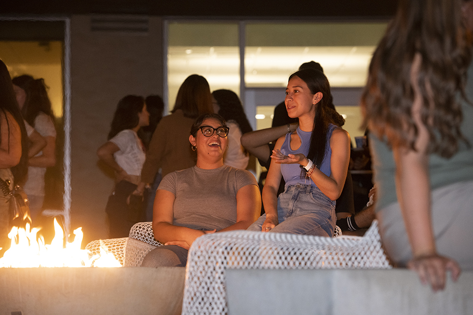 Two students sit in front of fire in fire pit.