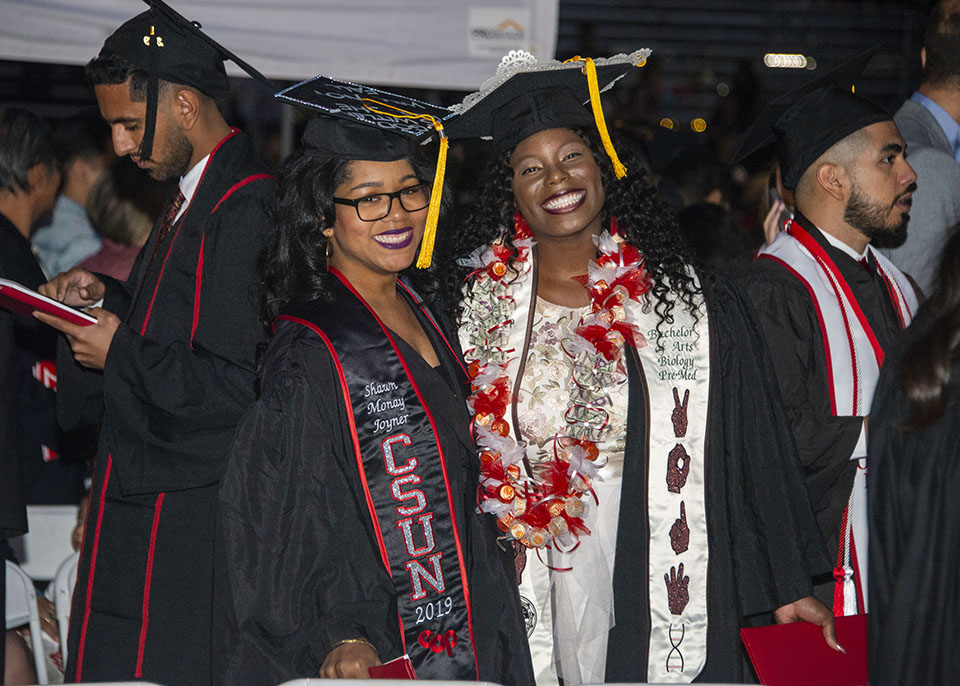 Two college graduates are wearing decorated graduation caps and smiling together after a graduation ceremony.