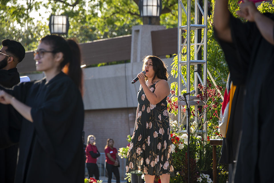 university student holds a microphone and sings on a stage at a graduation ceremony.