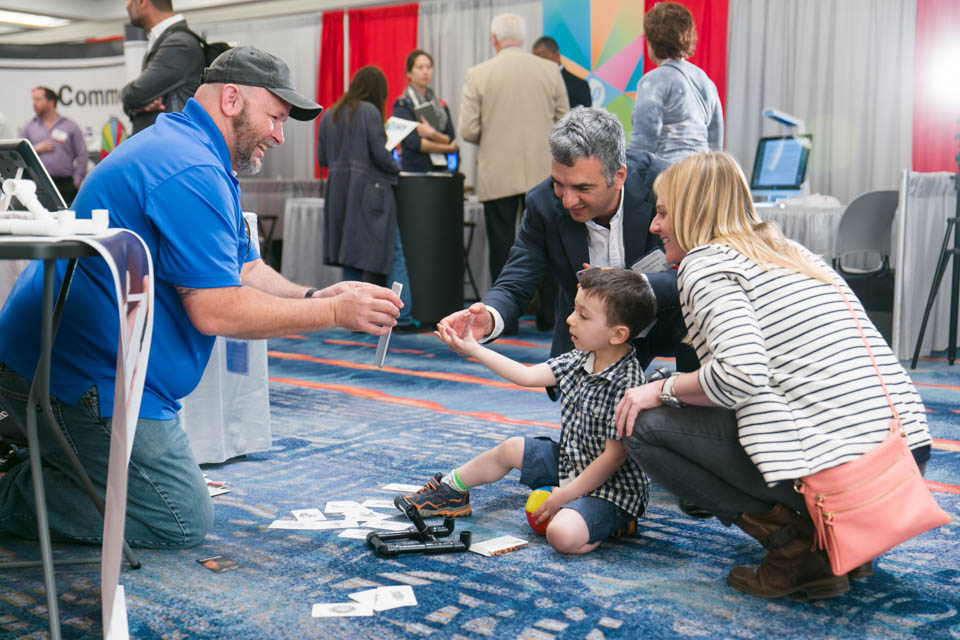 Exhibitor holds up an electronic tablet in front of a boy and his parents.