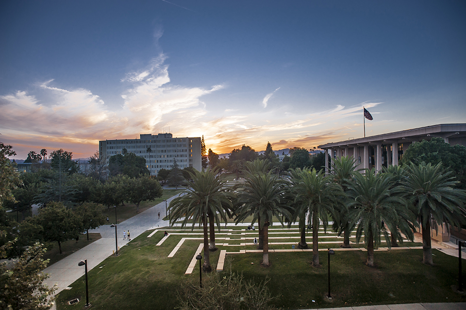 A shot of CSUN's campus at sunset, with the sun going down over the library, Sierra Tower and palm trees.