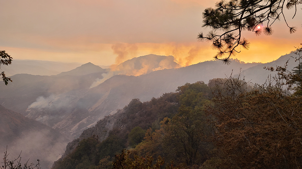 Landscape photo shows a red glow in the sky over smoky hills.
