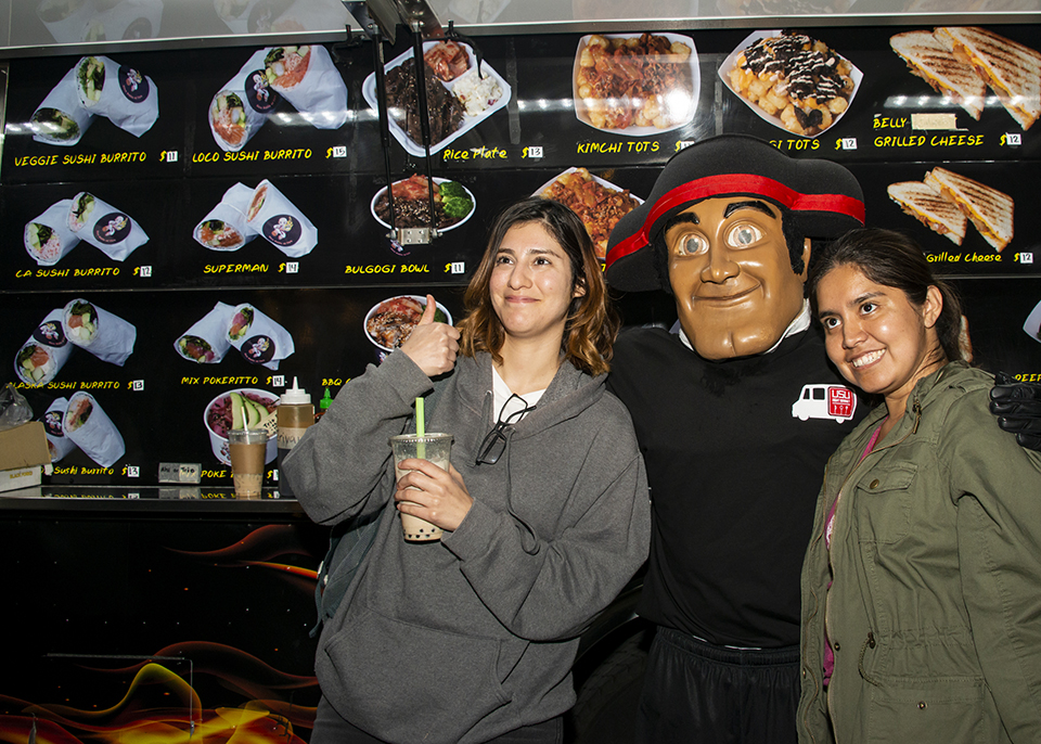 Two female students and Matty the matador posing for a photo infant of a food truck.