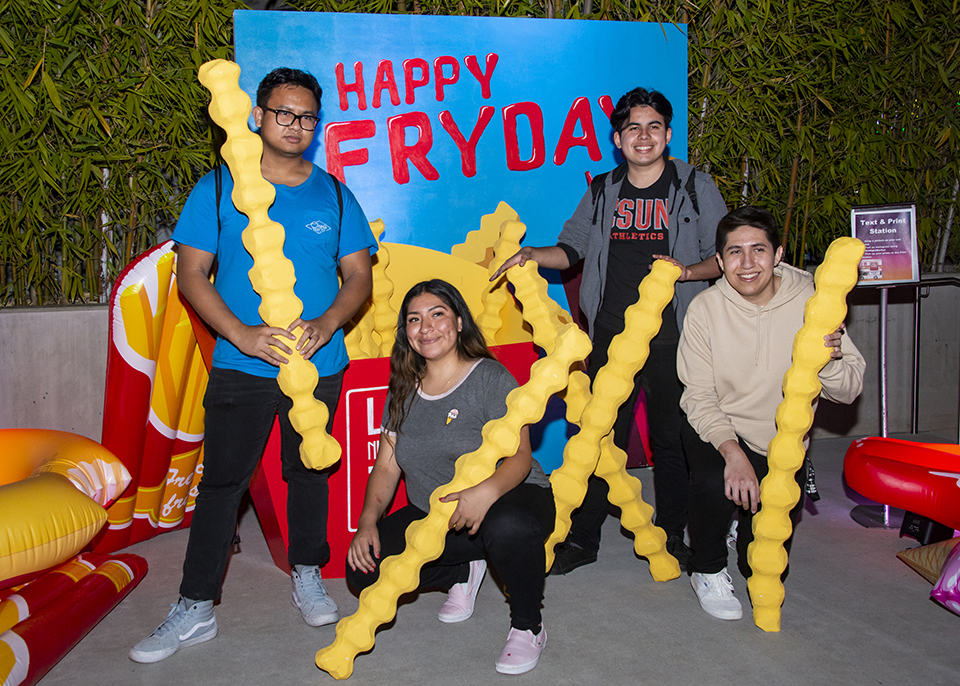 Three male and one female student holding life-sized French fries for a photo