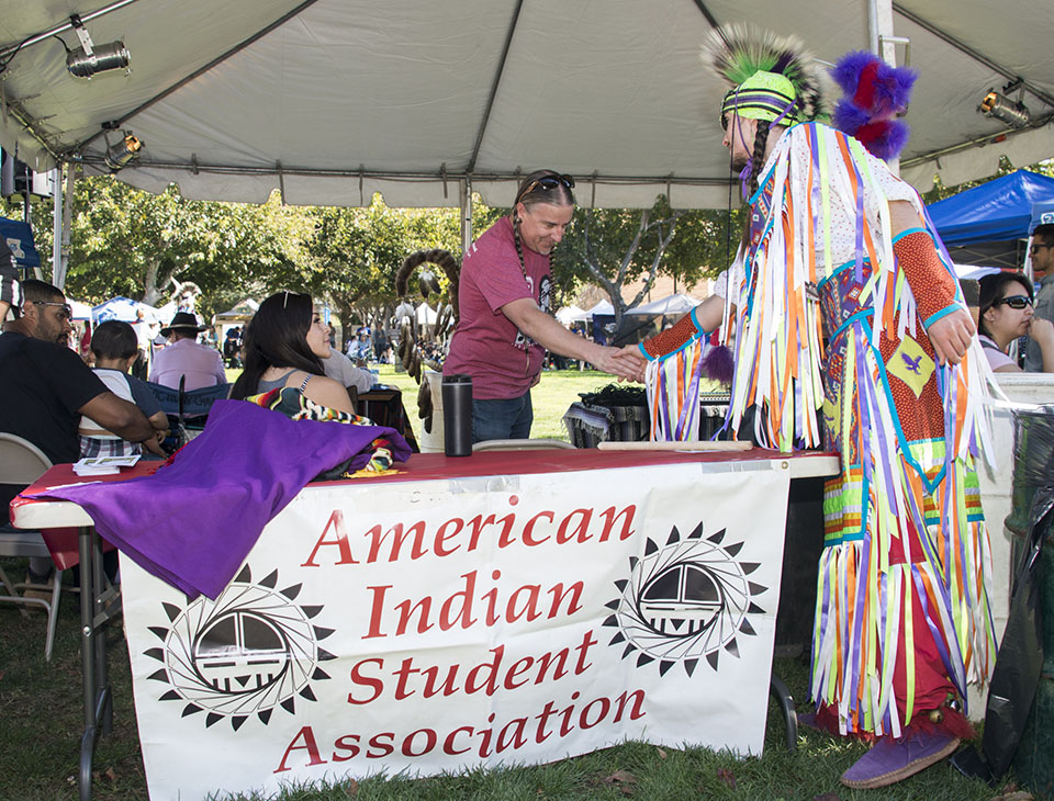 Two people getting over a table with a sign for CSUN's American Indian Student Association,