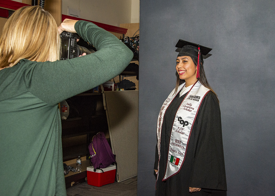 Young woman, in cap and gown, with a decorated sash, posing for a photo.