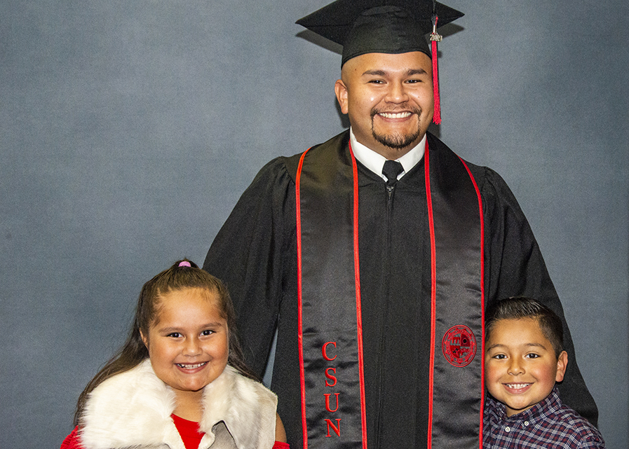 A man, in cap and gown, with his son and daughter, posing for a photo.