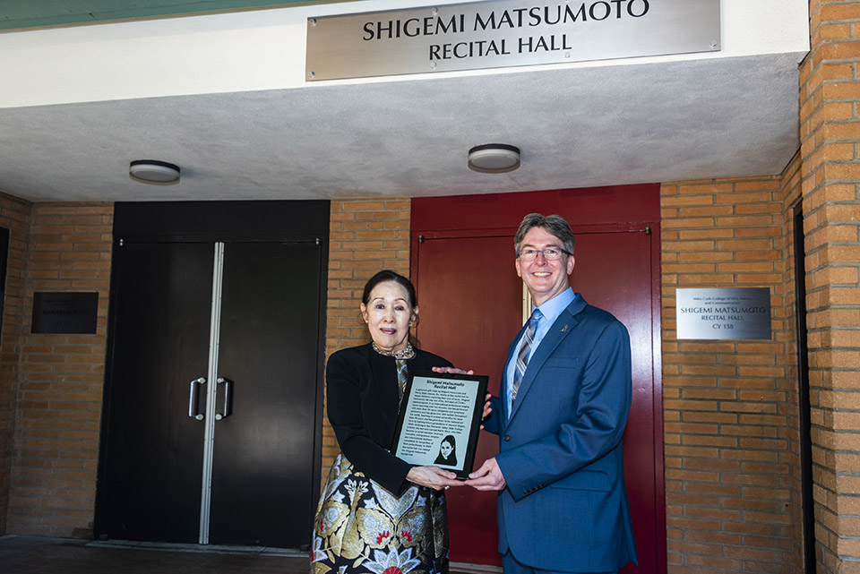 Mike Curb College of Arts, Media, and Communication Dean Dan Hosken presents Shigemi Matsumoto with a miniature plaque outside the Shigemi Matsumoto Recital Hall at CSUN.