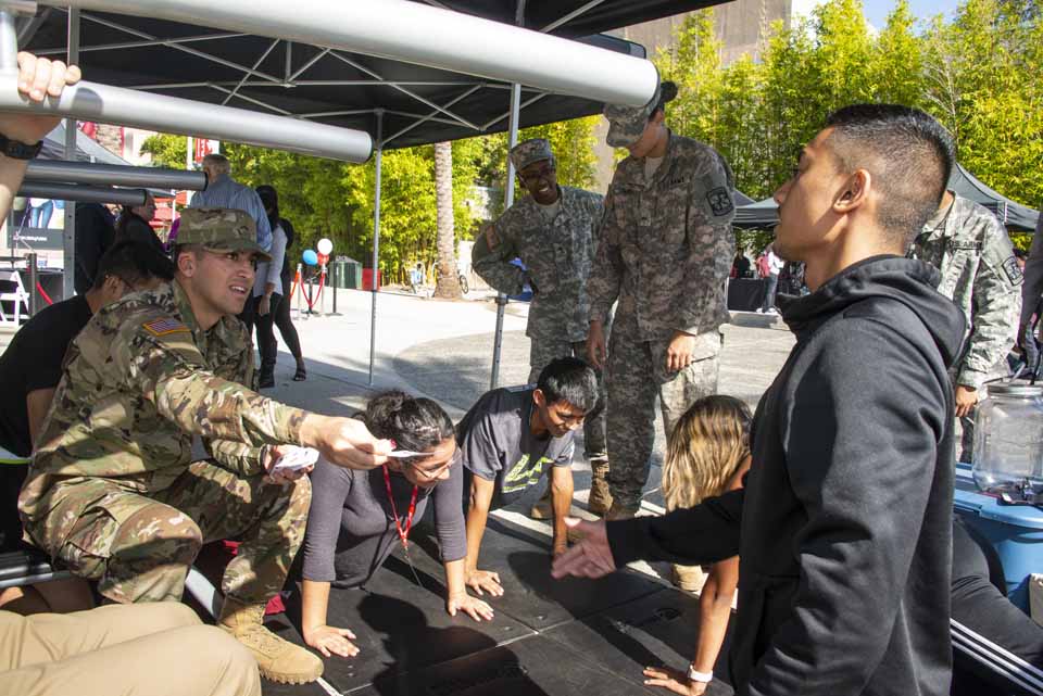 A student veteran hands out a card while students try military push-ups on CSUN's Plaza del Sol.