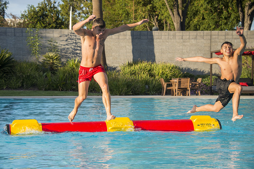 Two boys falling off a plastic log in a pool.
