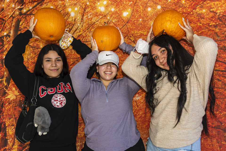 Three people pose holding pumpkins over their heads