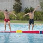 Two boys balancing on a plastic log in a pool.