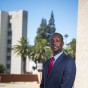 Portrait of Barrett Morris, standing on the CSUN campus with palm trees and Sierra Tower in the background on a sunny day.
