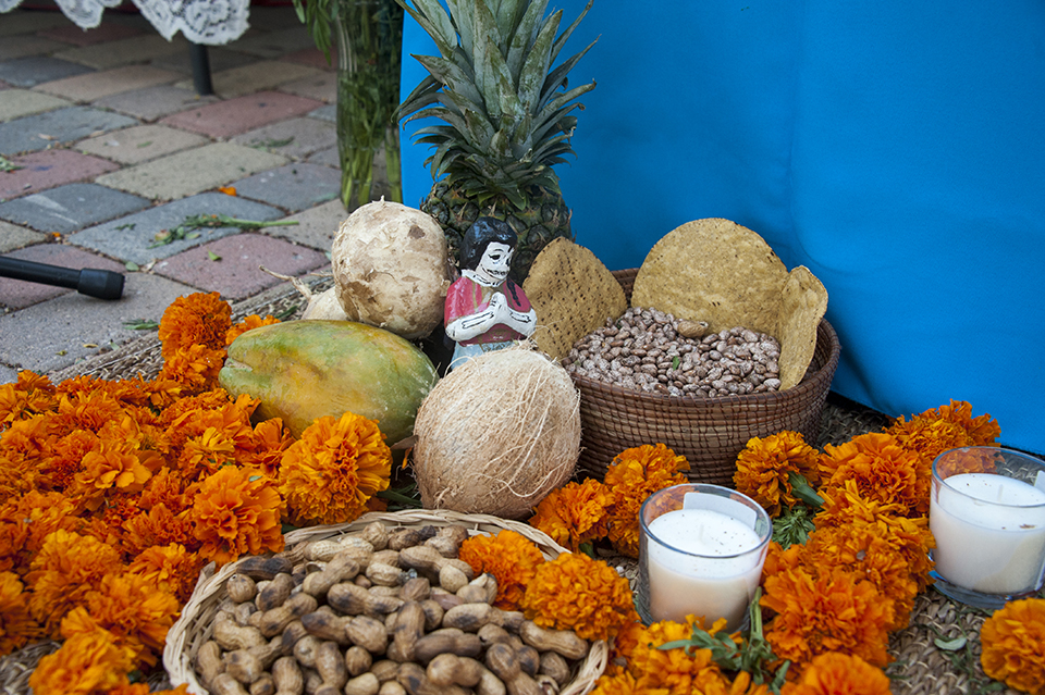 Orange flowers, fruit, candles, a skeleton figure and baskets of peanuts and beans decorate an altar.