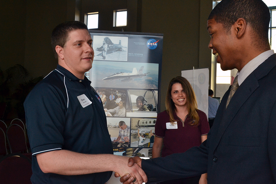 Barlow shakes hand of male NASA rep, female NASA rep smiles in background.