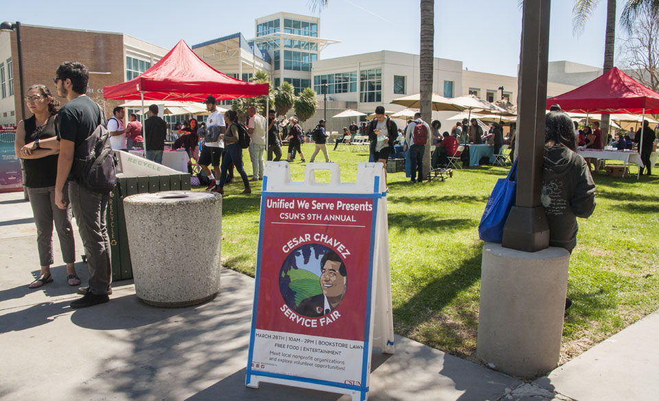 A-frame about Cesar Chavez Service Fair in front on Matador Bookstore lawn filled with people.