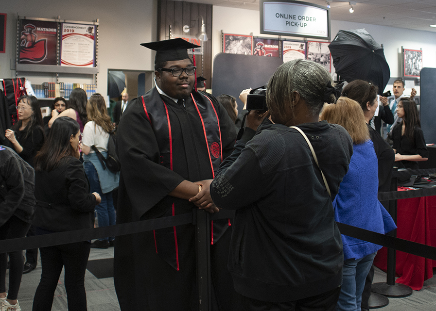Young man, in cap and gown, posing for a photo taken by his mother.