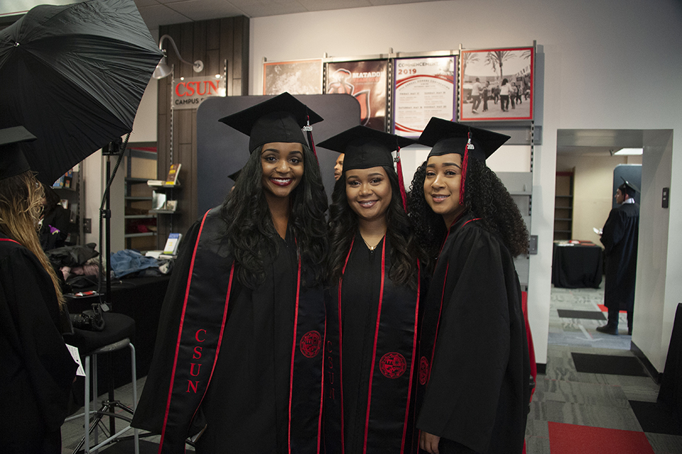 Three young woman, in cap and gown, huddle together for a photo.