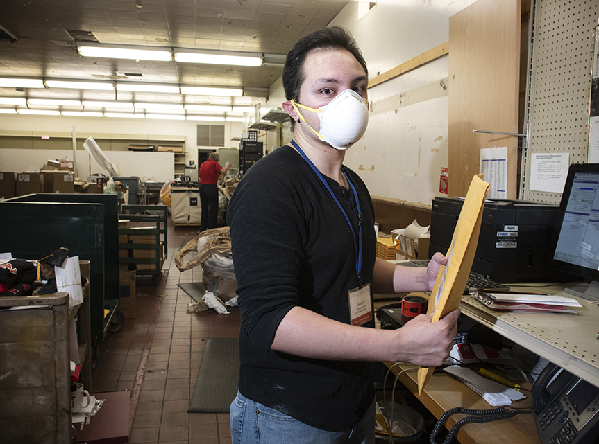 Trevor Iovine, wearing a face mask, handles a package in CSUN's bookstore,