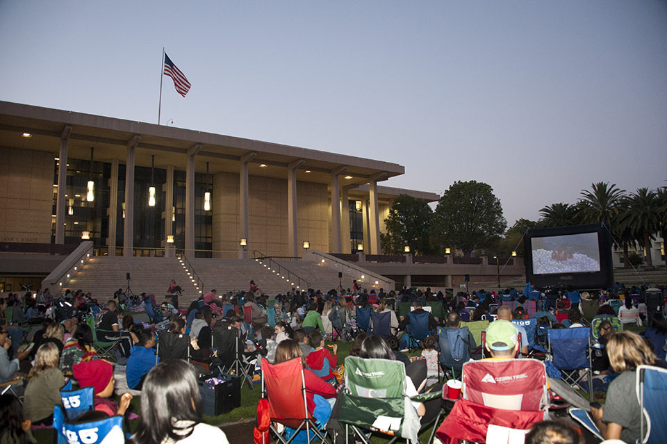 Crowd in lawn chairs on University Library Lawn facing an inflatable movie screen