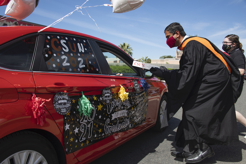 Man in commencement gown handing box to person in decorated car