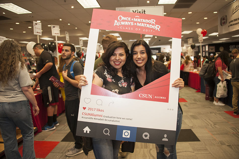 Two women pose with a CSUN alumni photo frame.