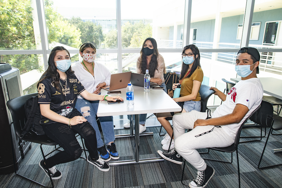 Five students wearing masks sitting around a table.