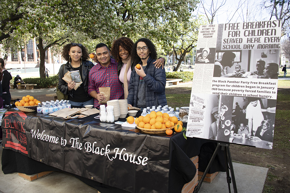 Department of Africana Studies Chair Theresa White poses with three students at a table celebrating the Black Panther Breakfast program.
