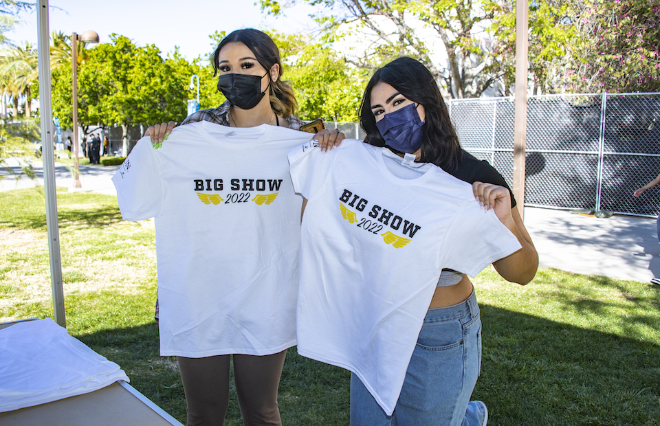 Two young women wearing masks display white t-shirts with 