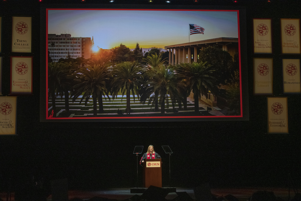 Erika D. Beck on stage with video monitor behind her showing view of CSUN